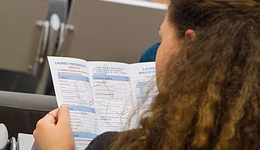 Studentessa ripresa di spalle che legge un depliant