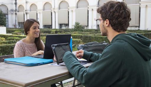 Studentessa e studente con computer seduti ad un tavolo uno di fronte all'altra