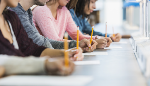 4 studenti in fila su una scrivania, con in mano una matita 