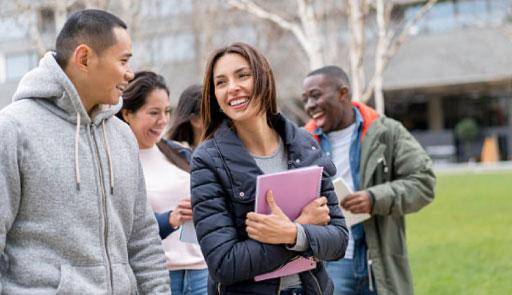 studenti e studentesse di etnie diverse chiacchierano sorridenti davanti a un campus universitario