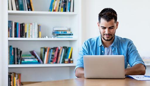 Photo by iStock / Getty Images Plus / DMEPhotography Giovane seduto alla scrivania consulta il computer